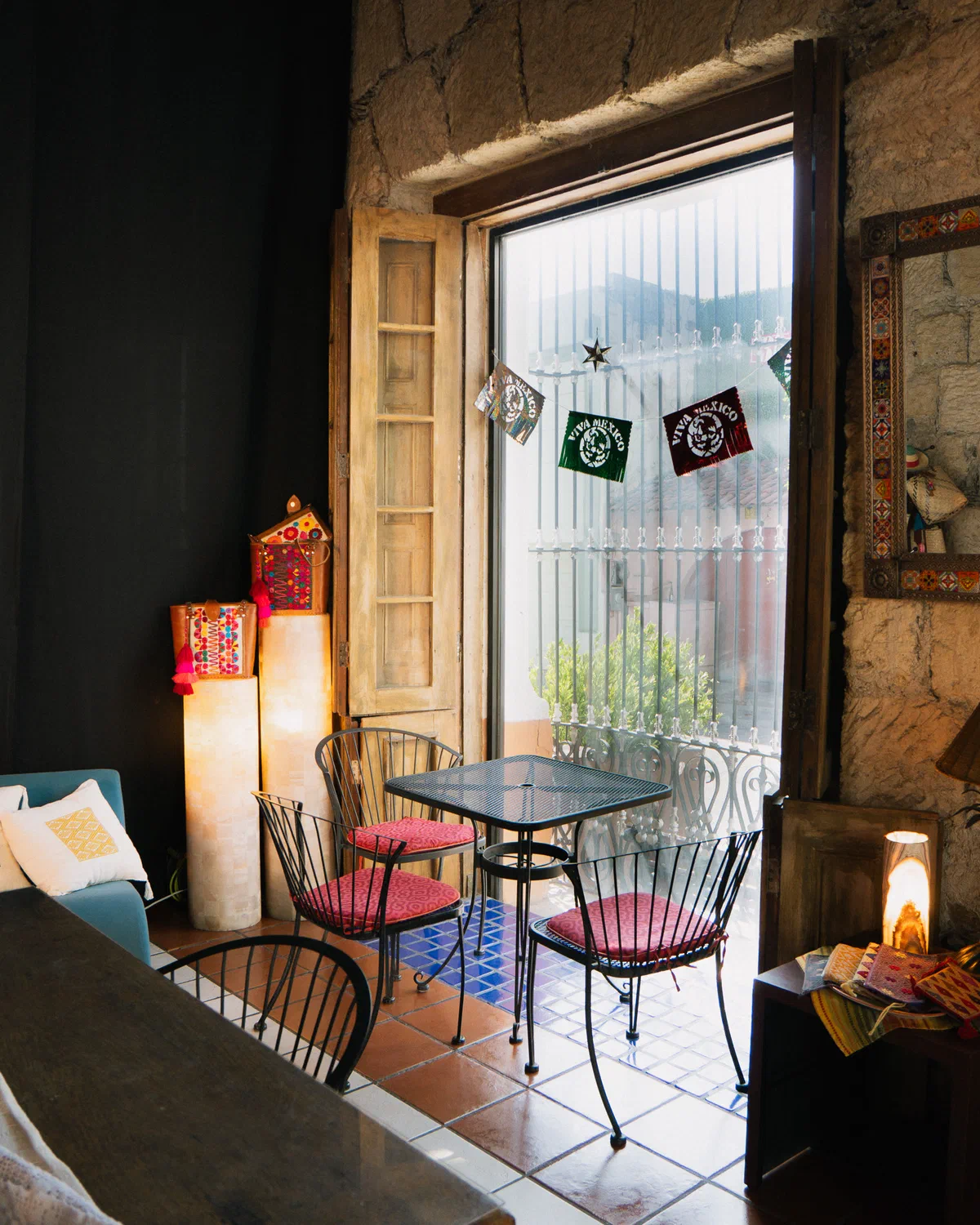 Interior de la cafetería Audaz con mesa de herrería, sillas rojas y ventanal con papel picado