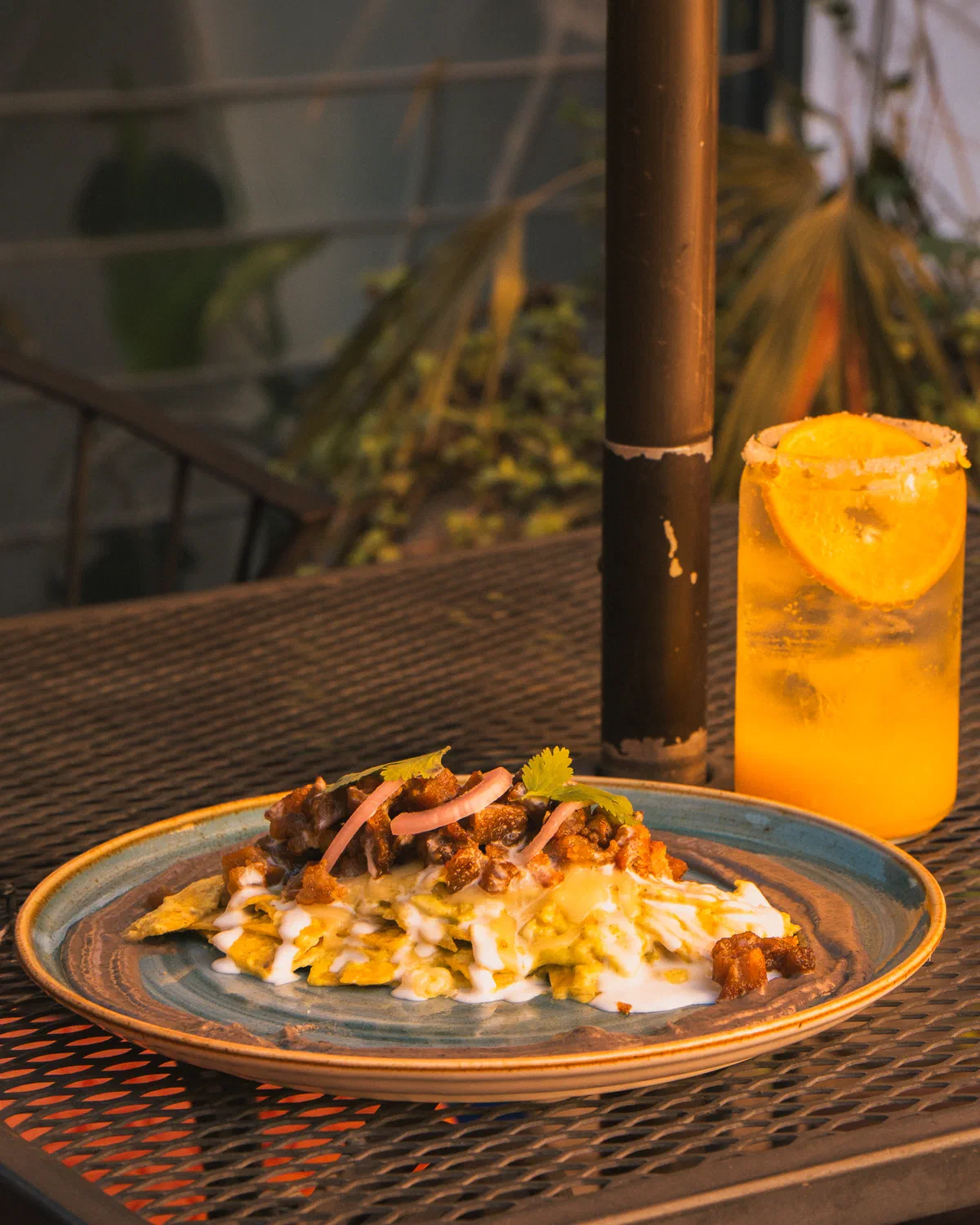 Platillo en plato de cerámica azul con bebida de naranja escarchada en la terraza de Audaz