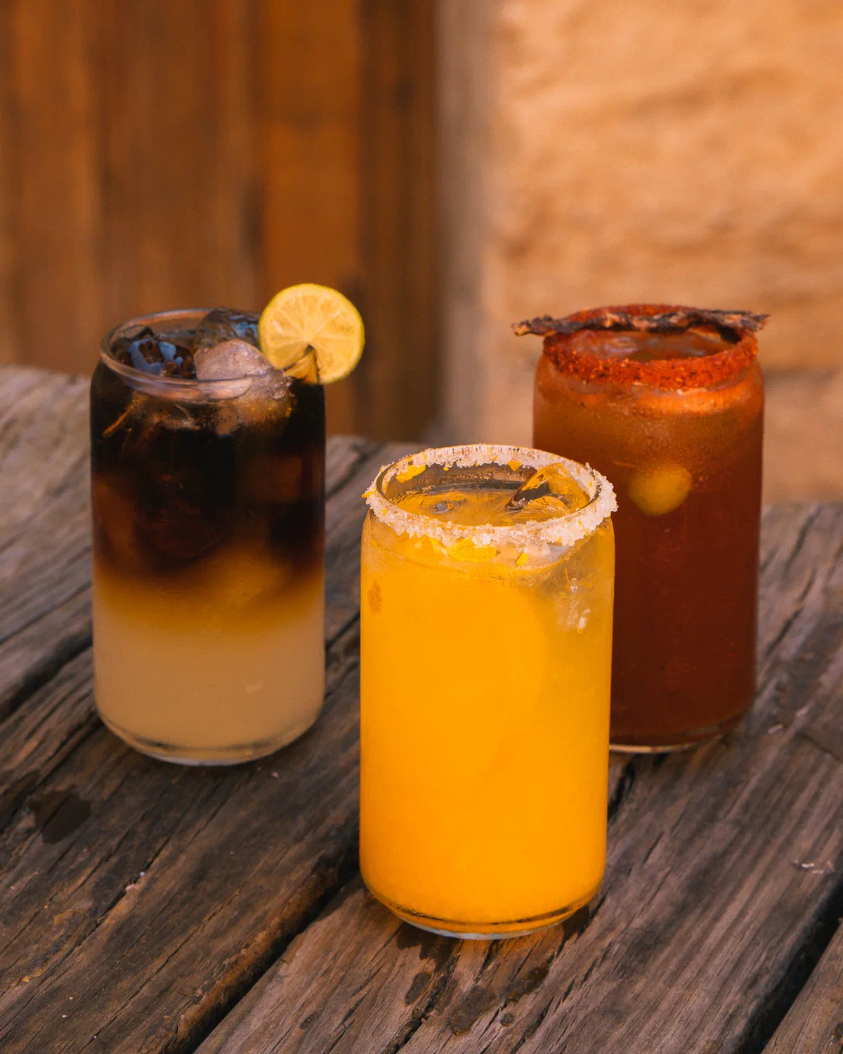 Tres bebidas de Audaz sobre mesa de madera: café en capas, bebida de naranja y bloody mary