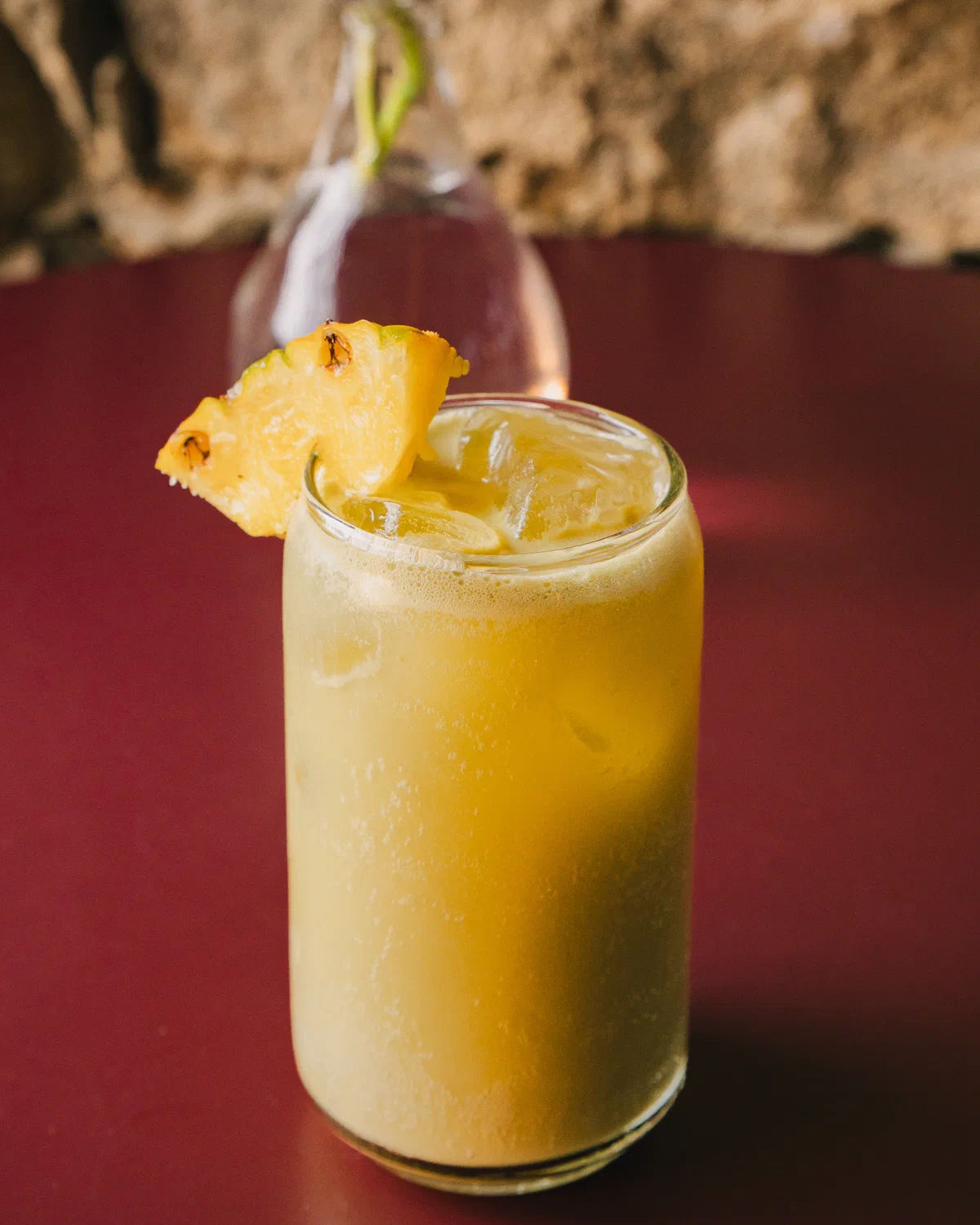 Bebida cremosa de piña con rodaja de piña asada sobre mesa roja