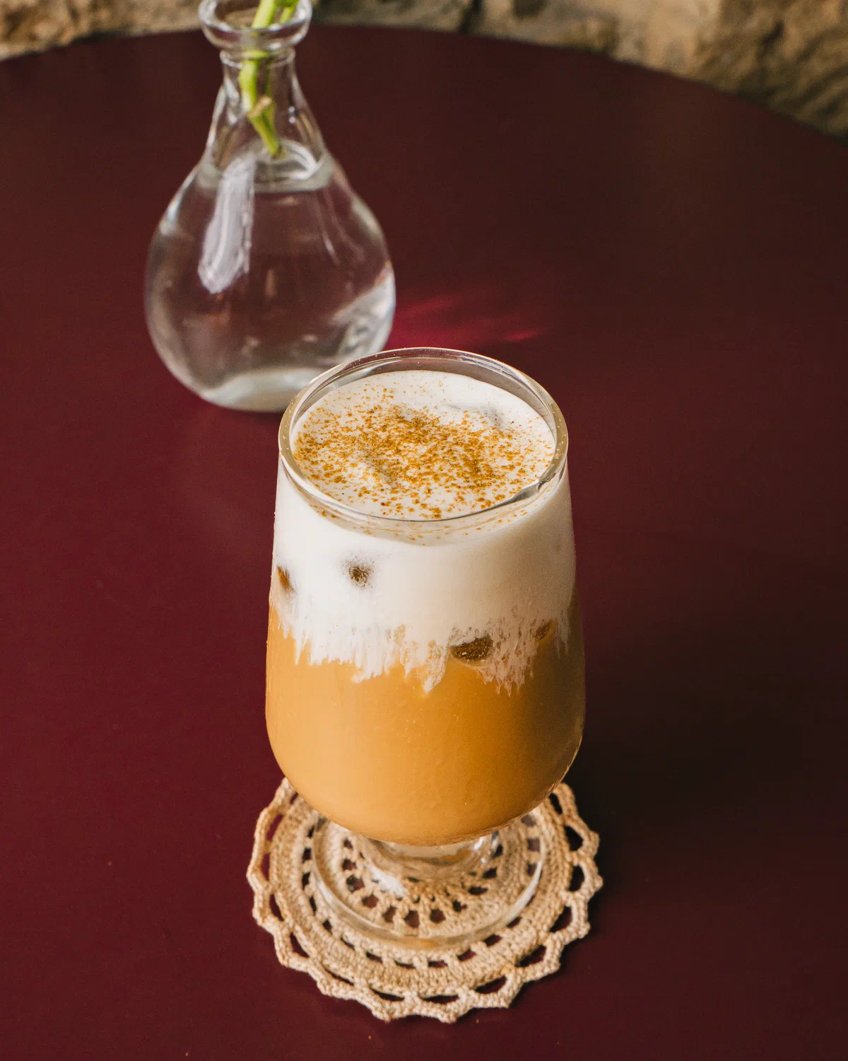 Café con espuma y canela en copa de vidrio sobre carpeta tejida