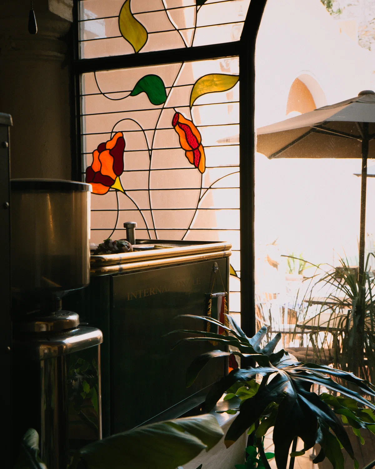 Barra de café con molino junto al vitral y plantas en Audaz