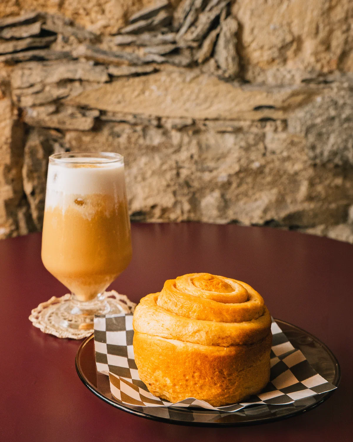 Café con espuma y rol de canela sobre papel a cuadros, cafetería Audaz