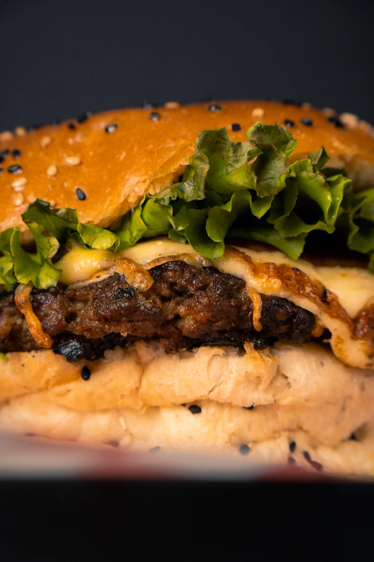 Primer plano de hamburguesa con carne a la parrilla, lechuga y queso derretido