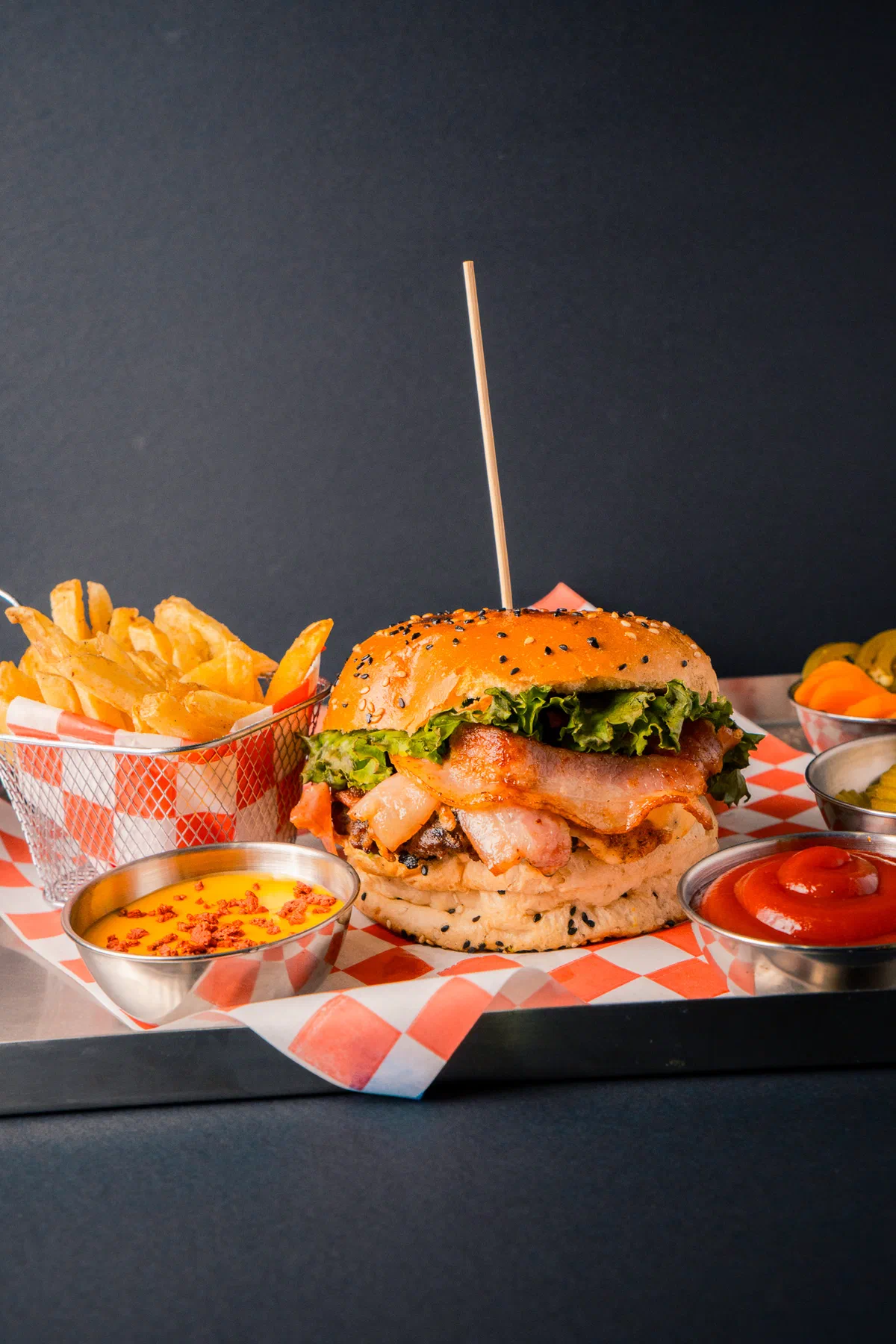 Hamburguesa con tocino, papas y salsas sobre charola