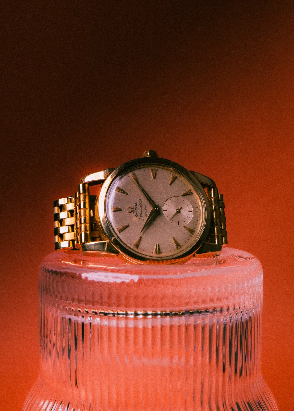 Reloj Omega dorado sobre pedestal de vidrio estriado con luz cálida