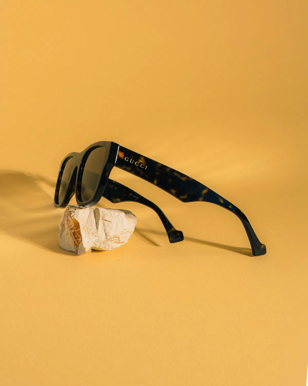 Lentes de sol Gucci sobre una piedra, fondo amarillo